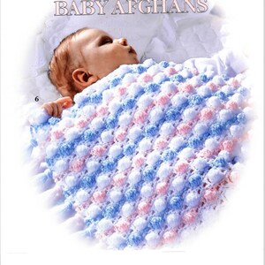 Puede incluir: Un bebé está envuelto en una manta de bebé de crochet blanca, azul y rosa con un punto de bobble texturizado. La manta tiene un patrón a rayas y está hecha de hilo suave.