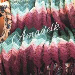 May include: A crocheted chevron throw blanket with a gradient of pink, green, and burgundy colours. The blanket has fringe on the edges.