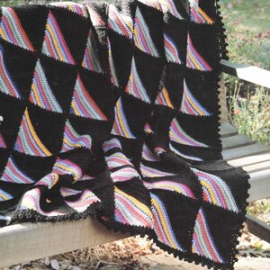 May include: A black crochet blanket with a colorful geometric pattern. The blanket is draped over a wooden bench.