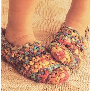 May include: Close-up of colorful, handmade slippers. The slippers are made of a textured, woven material in shades of red, yellow, blue, and green. The slippers are on a woven mat.