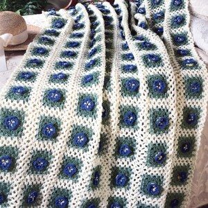 Puede incluir: Una manta de ganchillo con fondo blanco y un patrón floral azul y verde.