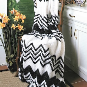 Pode incluir: Cobertor de crochet chevron preto e branco drapeado sobre uma cadeira de madeira. O cobertor tem uma superfície texturizada e irregular.