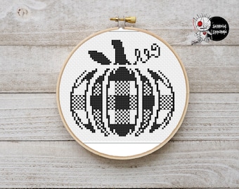 May include: A black and white cross-stitch pumpkin design in a wooden embroidery hoop. The pumpkin features a checkered pattern and is displayed against a light wood background. The text "SATIRICAL STITCHING" is visible in the upper right corner.