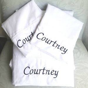May include: Three white pillowcases with the name "Courtney" embroidered in black cursive lettering. The top pillowcase has the name "Court" embroidered on it.