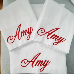 以下が含まれることがあります： 赤い筆記体で「Amy」と刺繍された白い枕カバーが3枚です。