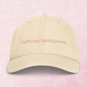 Könnte beinhalten: Eine beigefarbene Baseballkappe mit dem Text "cultivate faithfulness", der in einer gedeckten roten Schrift auf den Vorderteilen eingestickt ist. Die Kappe hat eine strukturierte Krone, einen gebogenen Schirm und genähte Ösen zur Belüftung.
