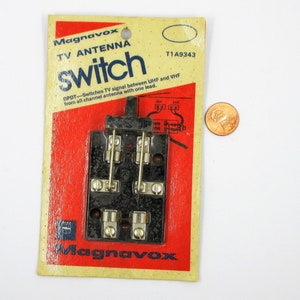 May include: A black Magnavox TV antenna switch with a red and white label. The label reads "Magnavox TV Antenna switch" and "DPDT-Switches TV signal between UHF and VHF from all channel antenna with one lead." The label also includes the model number "T1A9343".