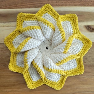 May include: Handmade crochet trivet in a starburst design. The trivet features a spiral pattern with white and yellow yarn. The outer edge and the inner spiral are outlined in a bright yellow color. This decorative item is perfect for protecting surfaces from hot dishes.