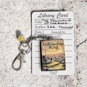 Pu&ograve; includere: Un portachiavi con un libro in miniatura de "La Compagnia dell'Anello" di J.R.R. Tolkien. Il libro &egrave; attaccato a una catena e un fermaglio color argento, con una perla dorata. &Egrave; inclusa anche una scheda della biblioteca con il titolo e l'autore.