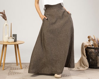 May include: A white sleeveless crop top with thin straps paired with a high-waisted, floor-length brown maxi skirt. The skirt features a wide waistband and side pockets, crafted from a textured fabric that falls in a loose, flowing silhouette.