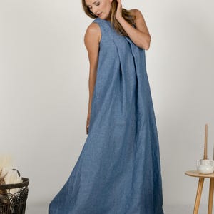 K&ouml;nnte beinhalten: Ein bodenlanges, &auml;rmelloses blaues Kleid mit einem plissierten Oberteil. Das Kleid besteht aus einem weichen, flie&szlig;enden Stoff und hat ein schlichtes, elegantes Design. Das Model tr&auml;gt das Kleid in einem Studio.