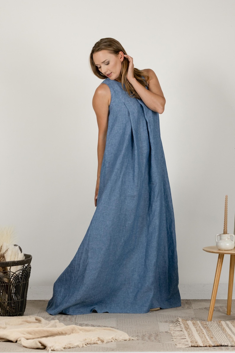 K&ouml;nnte beinhalten: Ein bodenlanges, &auml;rmelloses blaues Kleid mit einem plissierten Oberteil. Das Kleid besteht aus einem weichen, flie&szlig;enden Stoff und hat ein schlichtes, elegantes Design. Das Model tr&auml;gt das Kleid in einem Studio.