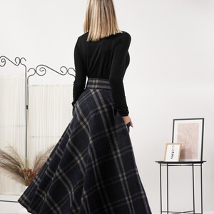 May include: A long, flared skirt with a plaid pattern in shades of navy, gray, and blue. The skirt is paired with a long-sleeved black top. The model is facing away from the camera.