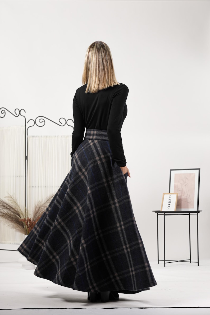 May include: A long, flared skirt with a plaid pattern in shades of navy, gray, and blue. The skirt is paired with a long-sleeved black top. The model is facing away from the camera.