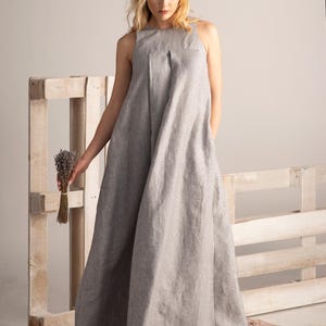 K&ouml;nnte beinhalten: Ein hellgraues, &auml;rmelloses Maxikleid mit hohem Ausschnitt. Das Kleid ist aus einem weichen, flie&szlig;enden Stoff gefertigt und hat eine lockere Passform. Das Model h&auml;lt ein B&uuml;ndel getrockneten Lavendels. Das Kleid eignet sich f&uuml;r l&auml;ssige oder formelle Anl&auml;sse.