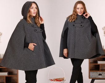 May include: A dark gray hooded cape featuring a double-breasted front design with four black buttons arranged in two horizontal rows. The garment has a high collar, side pockets, and a flared silhouette that extends to the mid-thigh area.