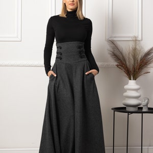 May include: A woman in a black turtleneck top and a high-waisted, charcoal grey maxi skirt. The skirt has a fitted waistband with decorative buttons and pockets. The outfit is a stylish ensemble.
