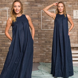K&ouml;nnte beinhalten: Ein &auml;rmelloses, marineblaues Maxikleid mit plissiertem Oberteil und Taschen. Das Kleid hat eine lockere Passform und einen bodenlangen Saum. Das Model tr&auml;gt das Kleid vor einer Backsteinmauer.