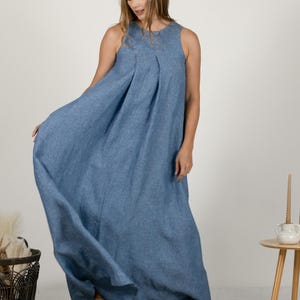 K&ouml;nnte beinhalten: Ein &auml;rmelloses, bodenlanges blaues Kleid mit einem plissierten Oberteil. Das Kleid ist aus einem flie&szlig;enden Stoff gefertigt und hat eine lockere Passform. Das Model tr&auml;gt beige Schuhe. Das Kleid eignet sich f&uuml;r l&auml;ssige oder halbformelle Anl&auml;sse.