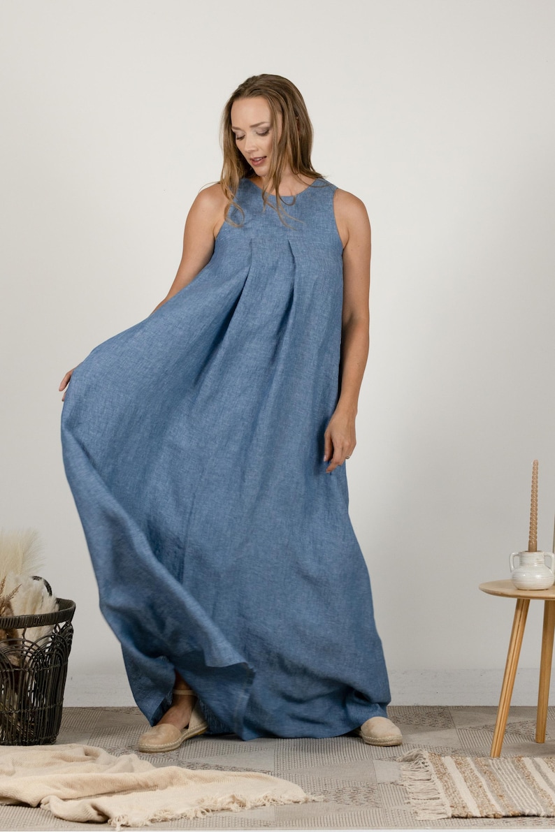 K&ouml;nnte beinhalten: Ein &auml;rmelloses, bodenlanges blaues Kleid mit einem plissierten Oberteil. Das Kleid ist aus einem flie&szlig;enden Stoff gefertigt und hat eine lockere Passform. Das Model tr&auml;gt beige Schuhe. Das Kleid eignet sich f&uuml;r l&auml;ssige oder halbformelle Anl&auml;sse.