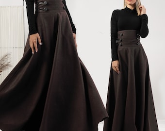 May include: A dark brown, high-waisted skirt with a wide waistband and decorative buttons. The skirt has a full, flowing A-line silhouette. The model is wearing a black long-sleeved top.