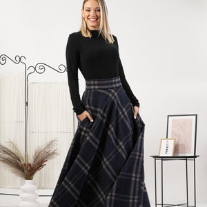 May include: A long, navy blue plaid skirt with pockets. The skirt is paired with a black long-sleeve top. The skirt features a classic plaid pattern in shades of navy, gray, and tan. The skirt is a full length, flowing style.