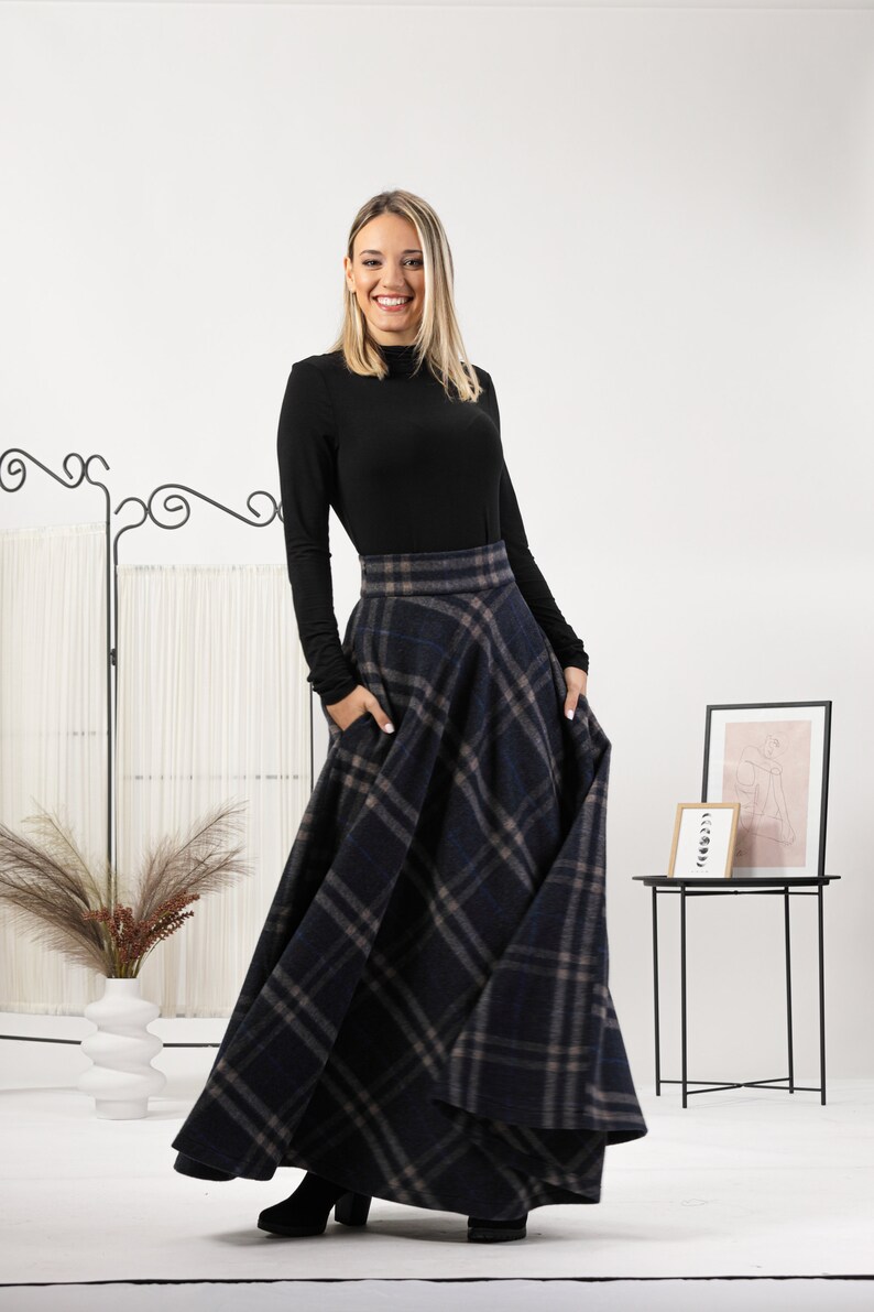 May include: A long, navy blue plaid skirt with pockets. The skirt is paired with a black long-sleeve top. The skirt features a classic plaid pattern in shades of navy, gray, and tan. The skirt is a full length, flowing style.