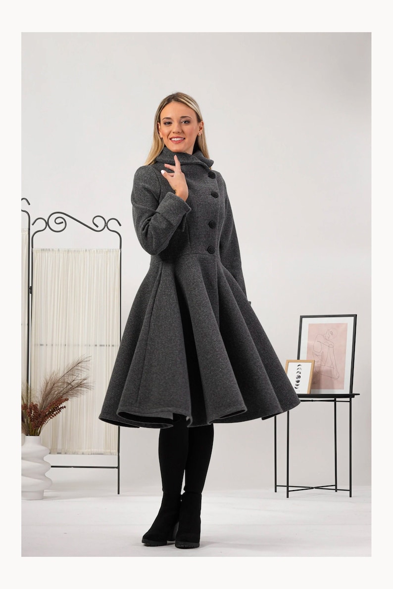 May include: A dark grey coat featuring a high collar, long sleeves, and a flared, full-skirted silhouette that extends to the knees. The garment is secured with a row of four large, round black buttons down the front, creating a structured look.