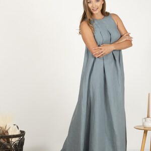 K&ouml;nnte beinhalten: Ein &auml;rmelloses, bodenlanges, hellblaues Kleid. Das Kleid hat ein gefaltetes Oberteil und einen flie&szlig;enden Rock. Das Model tr&auml;gt das Kleid. Das Kleid ist aus einem weichen Stoff gefertigt. Der Hintergrund ist wei&szlig;.