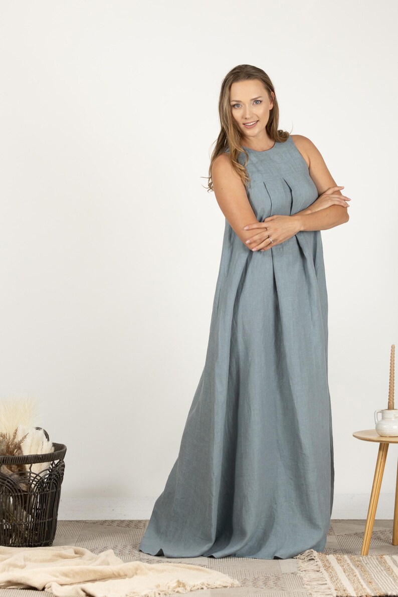 K&ouml;nnte beinhalten: Ein &auml;rmelloses, bodenlanges, hellblaues Kleid. Das Kleid hat ein gefaltetes Oberteil und einen flie&szlig;enden Rock. Das Model tr&auml;gt das Kleid. Das Kleid ist aus einem weichen Stoff gefertigt. Der Hintergrund ist wei&szlig;.
