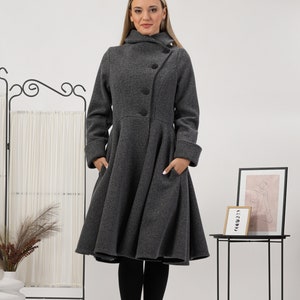 May include: A charcoal grey coat featuring a high collar, long sleeves with folded cuffs, and a flared, knee-length skirt. The coat has a button-down front closure with three visible black buttons and two side pockets integrated into the design.