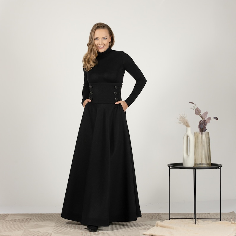 May include: A black outfit comprising a long-sleeved turtleneck top and a floor-length skirt. The top has a fitted bodice with decorative buttons. The skirt is full and flowing, with pockets. The ensemble is a classic, elegant style.