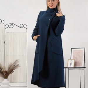 May include: A long, navy blue coat with a high collar and large, round buttons. The coat features two front pockets and a black trim along the edges. The coat is worn with black pants and boots.