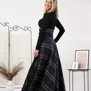 May include: A black long-sleeved top and a high-waisted, navy blue plaid skirt. The skirt has a classic plaid pattern in navy, grey, and brown. The outfit is suitable for various occasions.