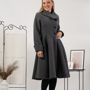 May include: A charcoal grey wool-blend coat featuring a wide folded collar, three large black buttons down the front, long sleeves with cuffs, and a flared, knee-length skirt silhouette. The coat is worn over black leggings and black ankle boots.