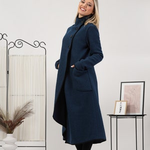 May include: A long, navy blue coat with a high collar and large buttons. The coat has pockets and a black trim along the edges. The model is wearing black boots. The coat is a stylish outerwear option.