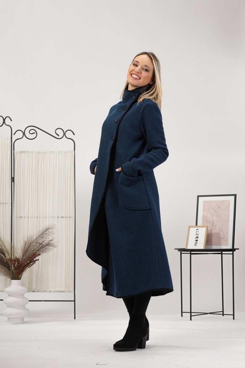 May include: A long, navy blue coat with a high collar and large buttons. The coat has pockets and a black trim along the edges. The model is wearing black boots. The coat is a stylish outerwear option.