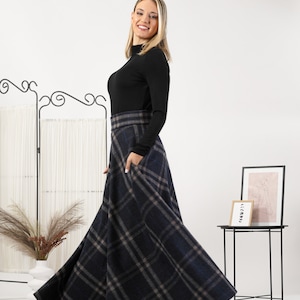 May include: A long, flowing plaid skirt in navy blue, gray, and light blue. The skirt has a wide waistband and pockets. The model is wearing a black long-sleeve top. The skirt is a stylish and versatile piece for any wardrobe.