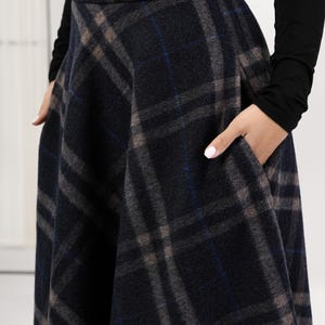 May include: A dark gray plaid skirt with a wide waistband and pockets. The plaid pattern includes shades of gray, blue, and brown. The skirt is made of a thick, woven fabric.