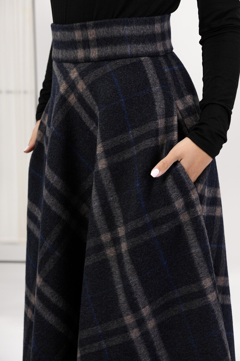 May include: A dark gray plaid skirt with a wide waistband and pockets. The plaid pattern includes shades of gray, blue, and brown. The skirt is made of a thick, woven fabric.