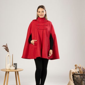 May include: A red hooded cape with a high collar and four button closures. The cape has a pocket on the left side and is made of a soft, warm fabric.