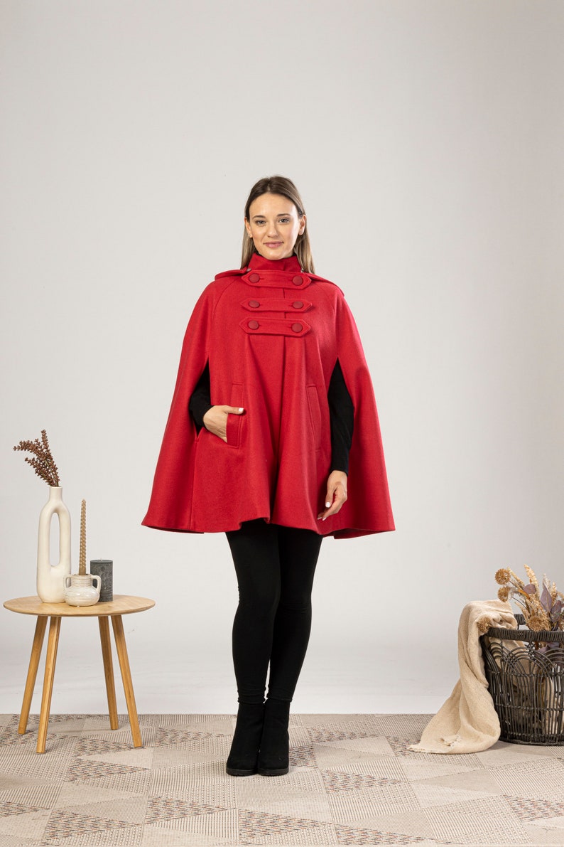 May include: A red hooded cape with a high collar and four button closures. The cape has a pocket on the left side and is made of a soft, warm fabric.