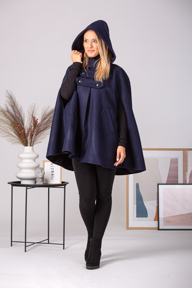 May include: A navy blue hooded cape with a double-breasted button closure. The cape is made of a soft, warm fabric and has a relaxed fit.
