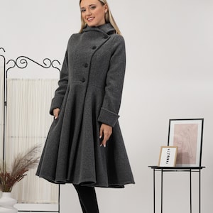 May include: A charcoal grey wool-blend coat featuring a high collar, long sleeves with folded cuffs, and a flared, pleated skirt silhouette. The coat has a diagonal button closure with three visible black buttons and side pockets.