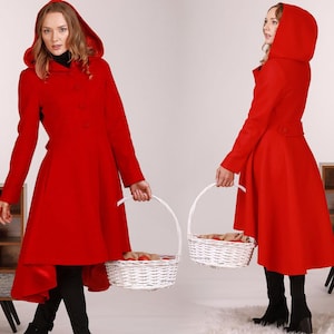 Pode incluir: Um casaco vermelho com capuz e uma bainha alta-baixa. O casaco tem fecho de botões e cinto. A modelo está segurando uma cesta de vime branca.