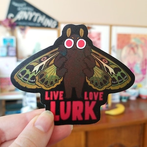 May include: A black and green moth sticker with red eyes and the text "Live Love Lurk" in pink.