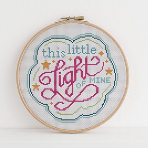 May include: A white embroidery hoop with a cross-stitch design that says "this little light of mine" in pink, blue, and yellow thread. The design is surrounded by small gold stars.