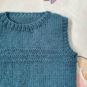 May include: A teal blue knitted sleeveless vest with a ribbed texture.