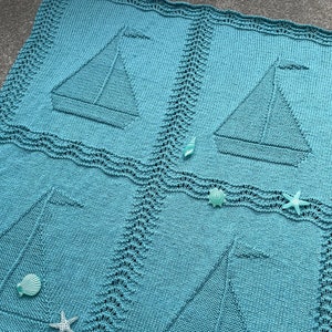 May include: A teal blue knitted baby blanket with four sailboats in a repeating pattern. The blanket is decorated with seashells and starfish.