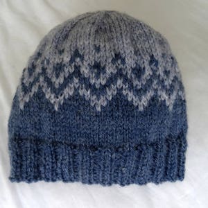 May include: A blue and gray knitted hat with a diamond pattern. The hat is made of soft yarn and has a fold-over brim.